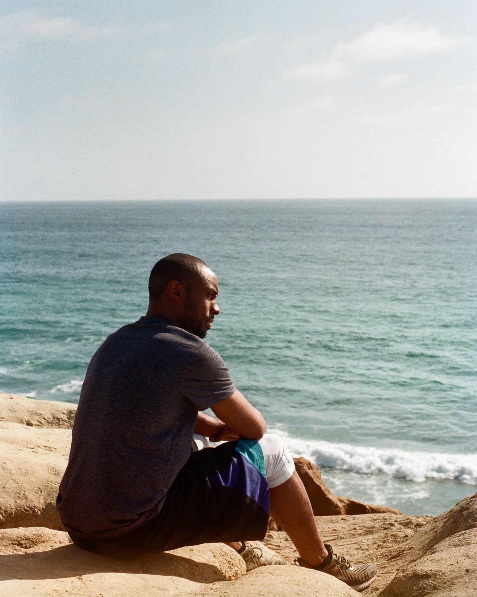 Q Burdette sitting on coastal rocks looking out to the Pacific