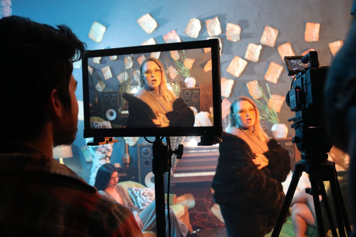 Q directing at the monitor with talent on set