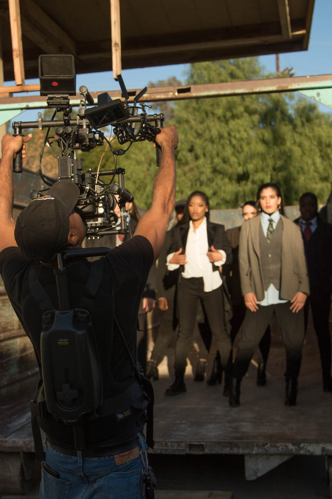 DP holding an overhead camera rig as performers walk into frame in golden light